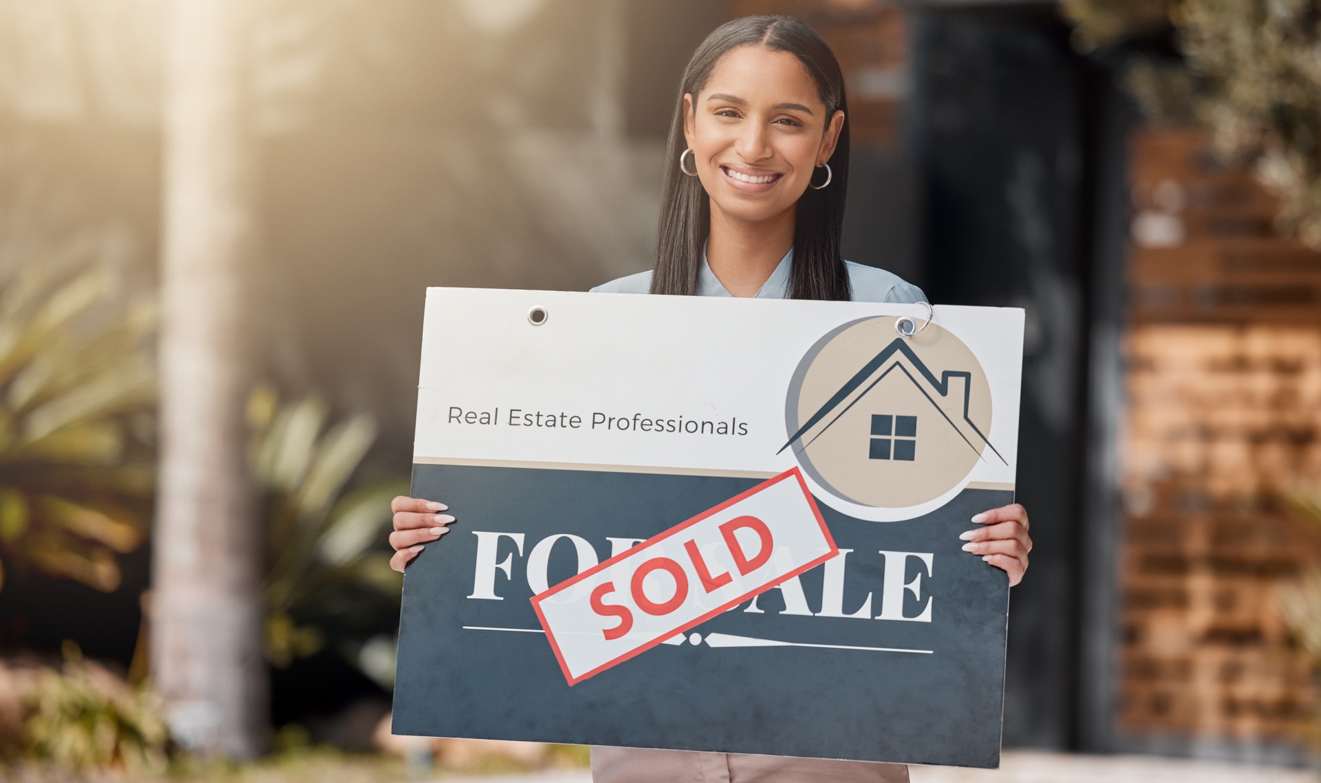 Shot of a real estate agent standing next to a sold sign outside